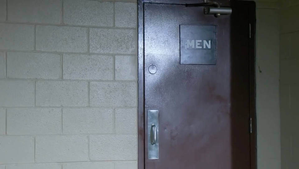 Still from "Caught" - An outside view of a public restroom door