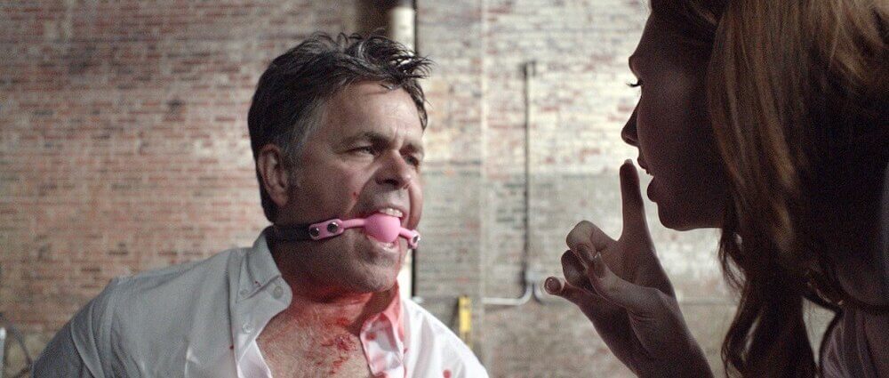 Still from "Conversion Therapist" - Ira is tied up, tortured, with ball gag while Tanya taunts him