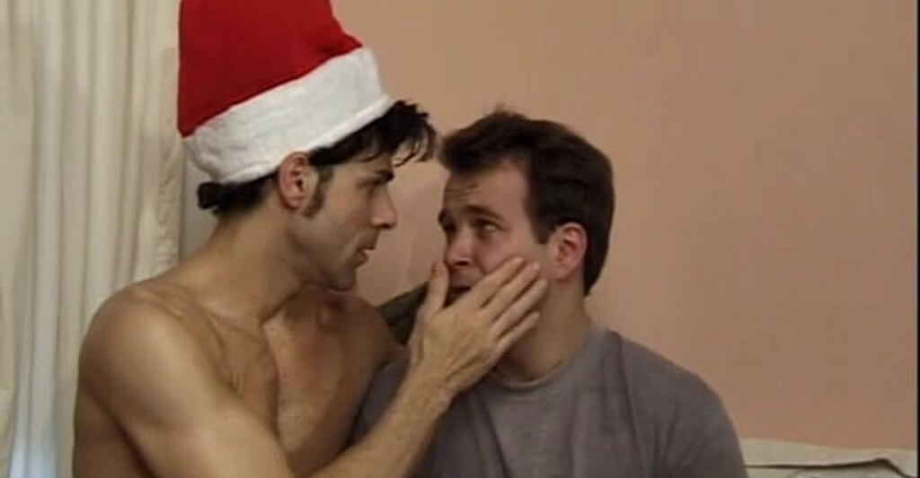 Still from Still from “Visions Of Sugarplums” - Bruce, shirtless and wearing a Santa hat, consoles his boyfriend Joey