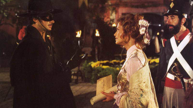 Zorro The Gay Blade 5 Still from "Zorro: The Gay Blade" - Charlotte, dressed in period dress, confronts Diego, who's wearing Zorro's iconic black outfit, hat, and mask
